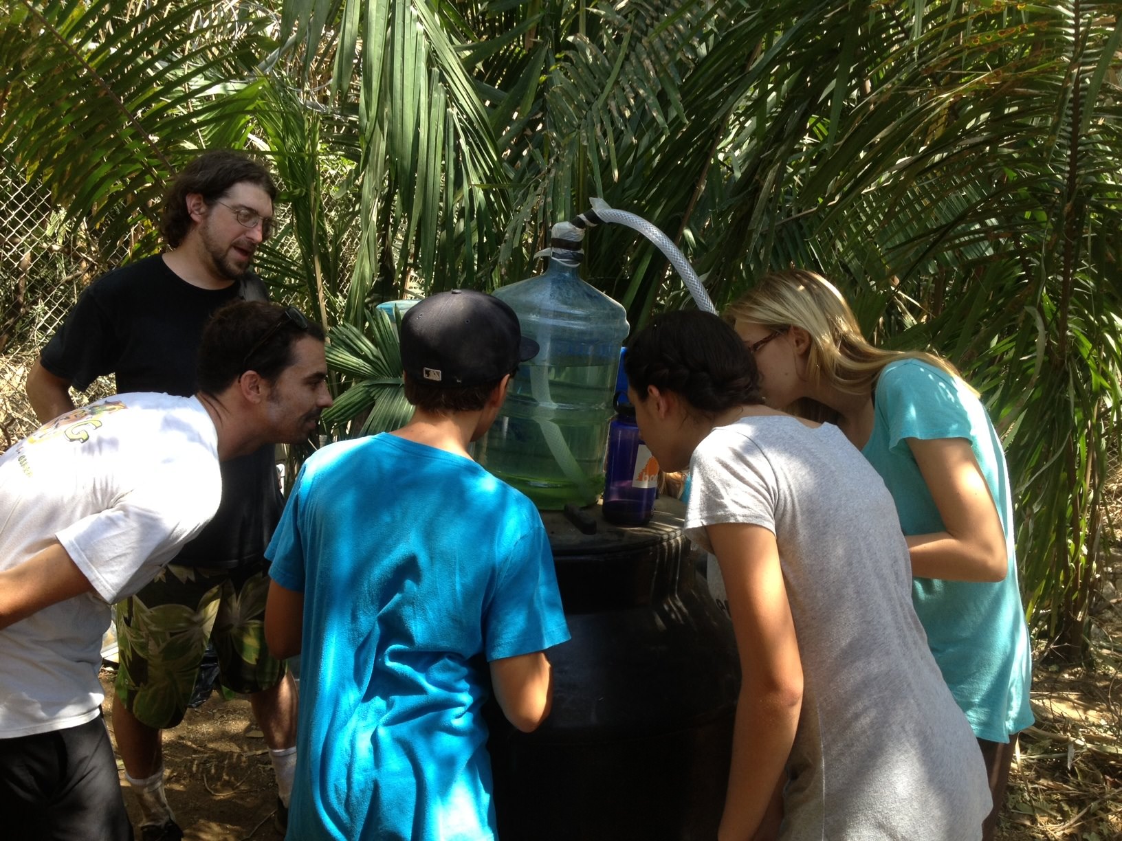Interested students peer intently at the biodiesel producer, while Instructor Nico presumably attempts to smell it. 
